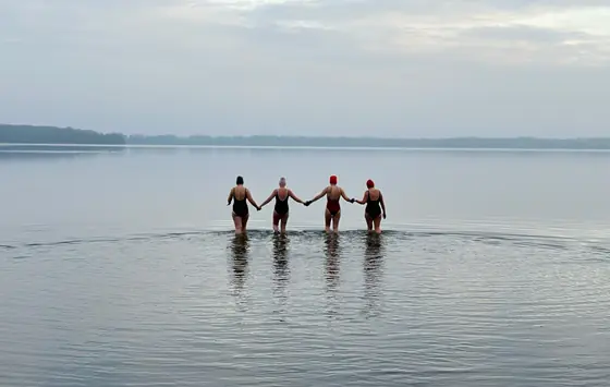 Vier Teilnehmerinnen gehen Hand in Hand ins kalte Wasser des Wolziger Sees